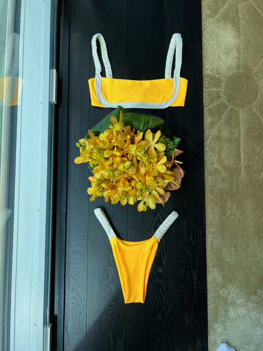 The Dandelion Bikini, a sporty and stylish choice for sun-soaked days. Featuring a cheerful yellow base with cream detailing, this bikini is designed for both comfort and flair. The scrunchy straps provide a secure fit while adding a trendy touch, making it perfect for tanning or beach activities. Its practical design ensures you can move freely without sacrificing style. Embrace summer vibes with The Dandelion Bikini, where sporty meets chic in one vibrant package!