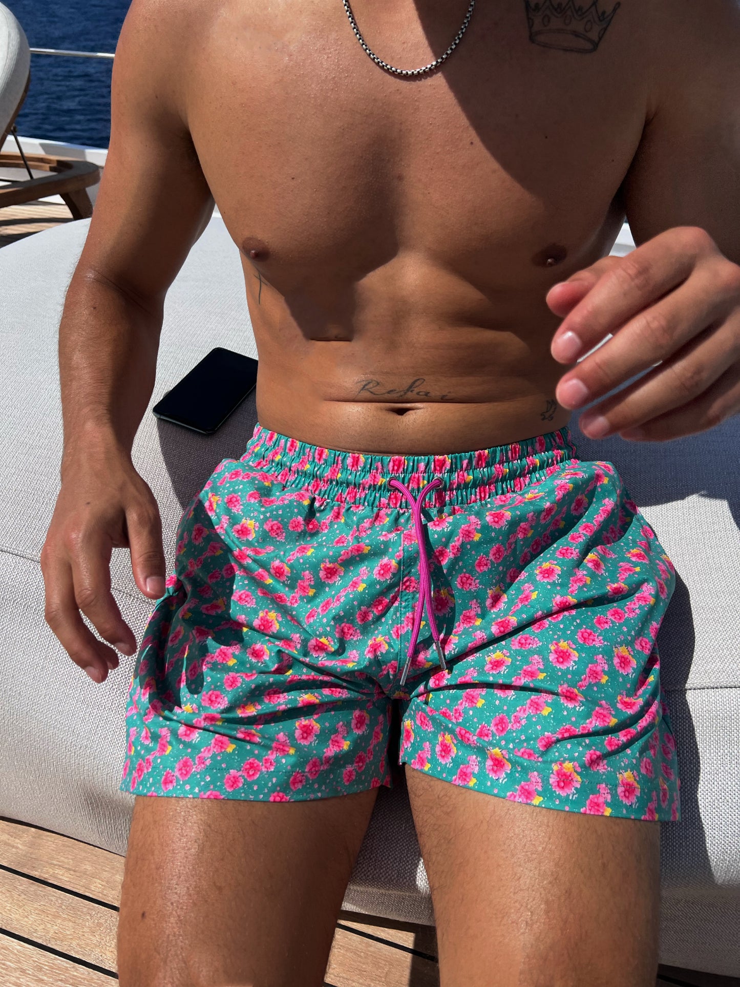 The Syros Short, your perfect companion for swimming and lounging in style. These versatile shorts feature a vibrant teal base adorned with eye-catching pink florals, capturing the essence of hot summer days. Designed with convenience in mind, they include pockets for ample storage of your essentials. The customizable fit ensures comfort whether you're at the beach or poolside. Embrace the summer vibe with The Syros Short, where fashion meets functionality for all your sunny adventures!