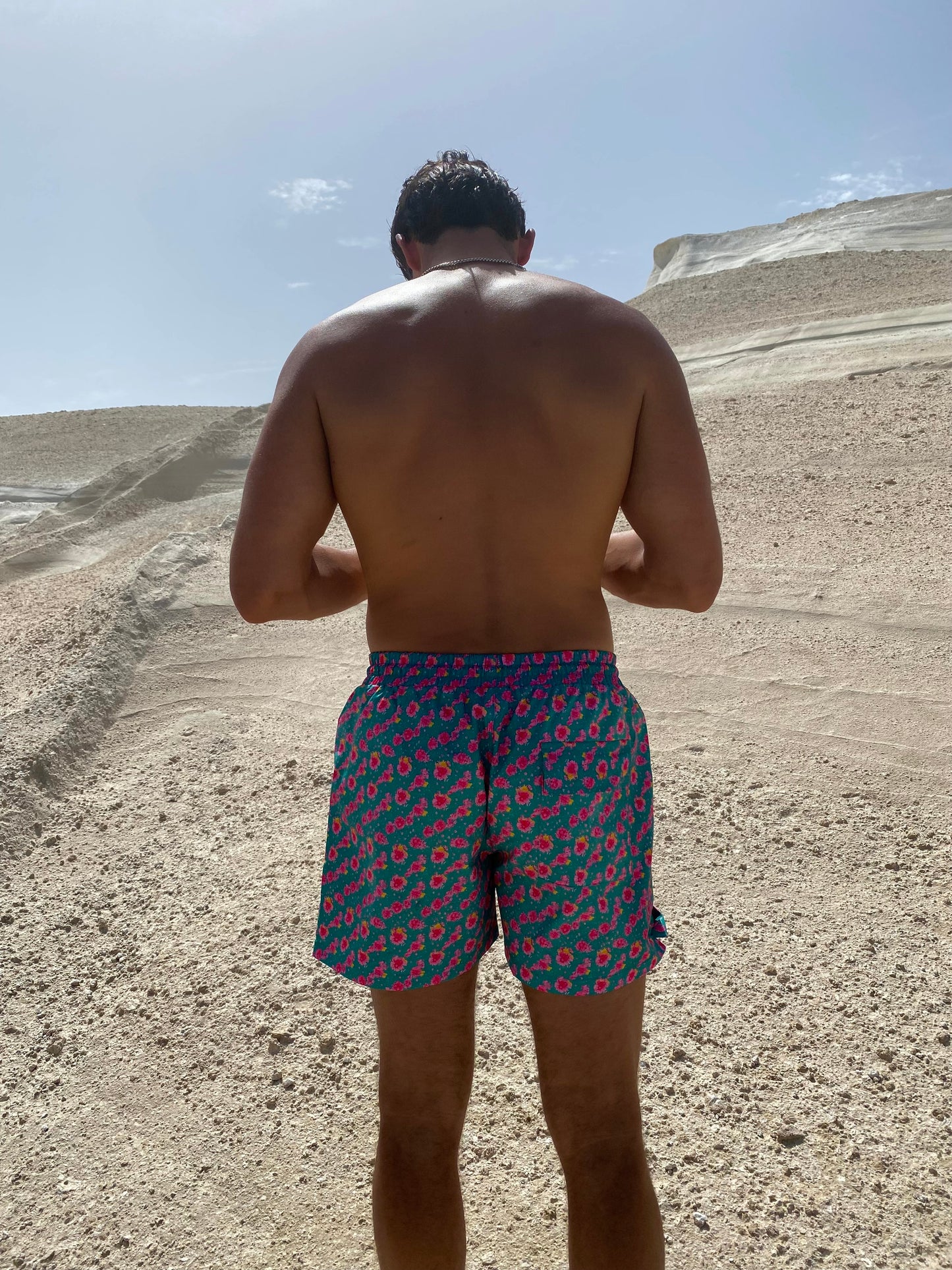 The Syros Short, your perfect companion for swimming and lounging in style. These versatile shorts feature a vibrant teal base adorned with eye-catching pink florals, capturing the essence of hot summer days. Designed with convenience in mind, they include pockets for ample storage of your essentials. The customizable fit ensures comfort whether you're at the beach or poolside. Embrace the summer vibe with The Syros Short, where fashion meets functionality for all your sunny adventures!