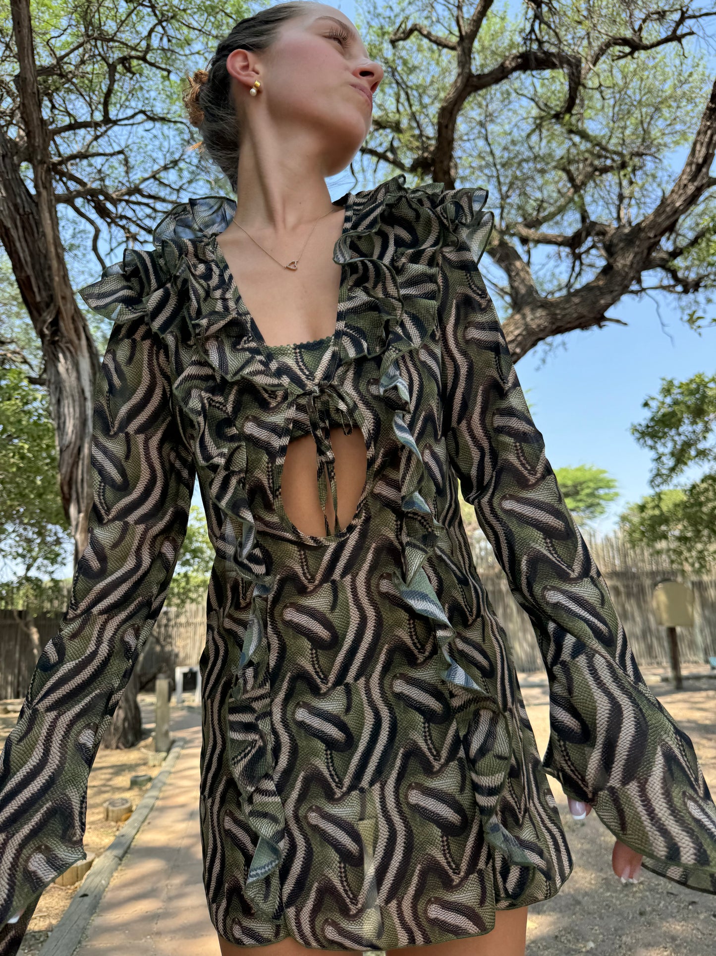 The Jungle Chiffon Dress, a stunning snake-print mini dress crafted from our signature lightweight chiffon. Designed to keep you looking hot while feeling cool, this dress features playful ruffle detailing and a center string tie for a flirty touch. Perfect for making a statement, it embodies the spirit of the queen of the jungle, allowing you to embrace your wild side with elegance. Whether you're lounging by the pool or enjoying a night out, The Jungle Chiffon Dress is your go-to for effortless style!