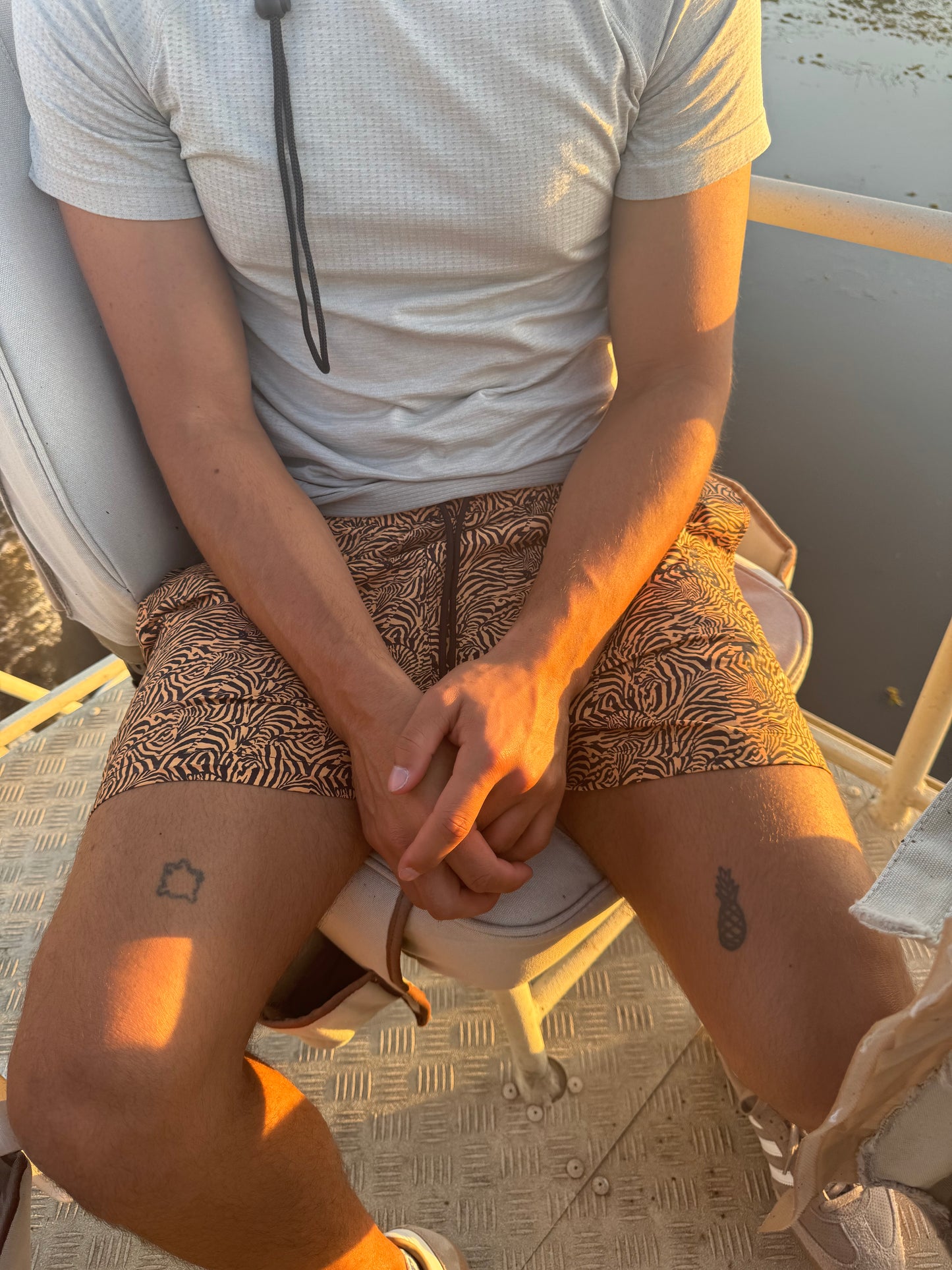 A photo showcases a male model sitting outdoors, wearing tiger print swim shorts during his vacation in South Africa. The bold pattern adds a stylish flair to his look. His comfortable pose emphasizes the versatility of the shorts, demonstrating their suitability for lounging by the pool, strolling along the beach, or enjoying casual outdoor activities. The image captures the essence of a relaxed yet fashionable vacation style, perfectly suited for the adventurous spirit of a South African getaw