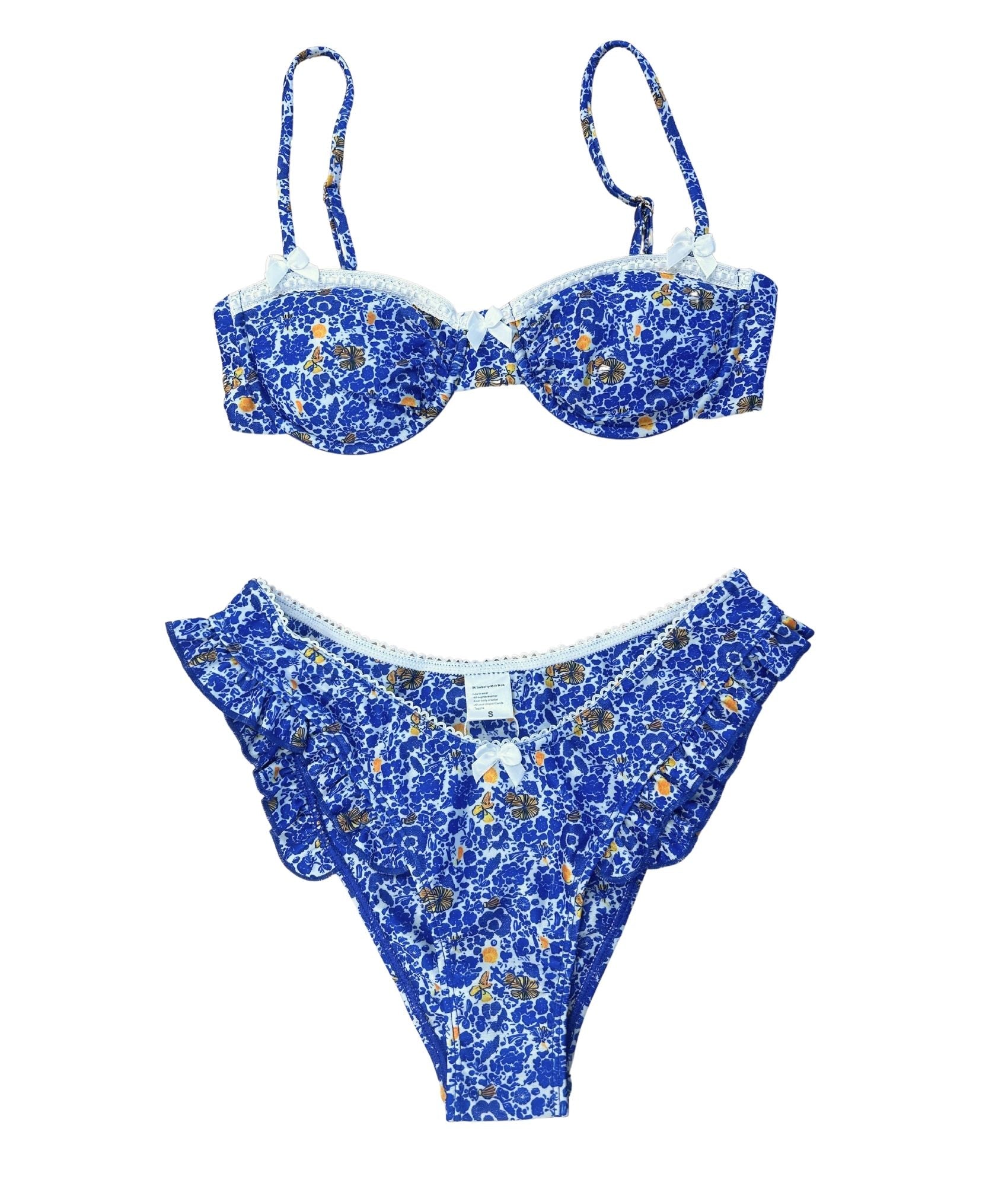 The Mykonos Bikini is a stunning blend of bold and sweet styles, inspired by the beauty of Greece. Featuring a charming floral design in vibrant blues, sunny yellow, and classic white, this bikini is perfect for making waves at the beach. Delicate white lace trim and a playful bow detail add a romantic touch, while its flattering fit enhances your curves. Lightweight and stylish, this timeless piece is an essential for your summer wardrobe, ensuring you look effortlessly chic!