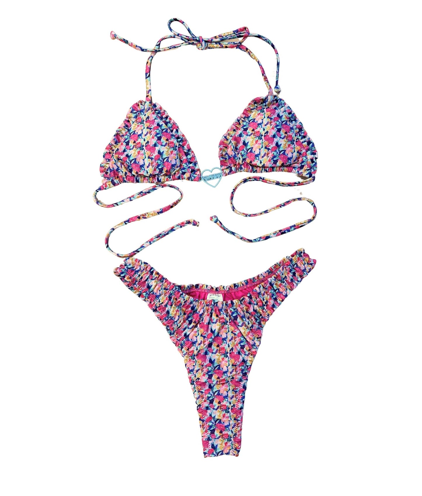 The Naxos Bikini, featuring a stunning floral print in vibrant purples, pinks, and blues. This bikini combines elegance and comfort, highlighted by a charming heart logo charm that adds a touch of sophistication. The unique scrunch detail enhances its flattering silhouette, ensuring you look and feel your best. Perfect for sun-soaked days by the beach or pool, this bikini captures the grace of island living while providing a stylish fit for every body type.