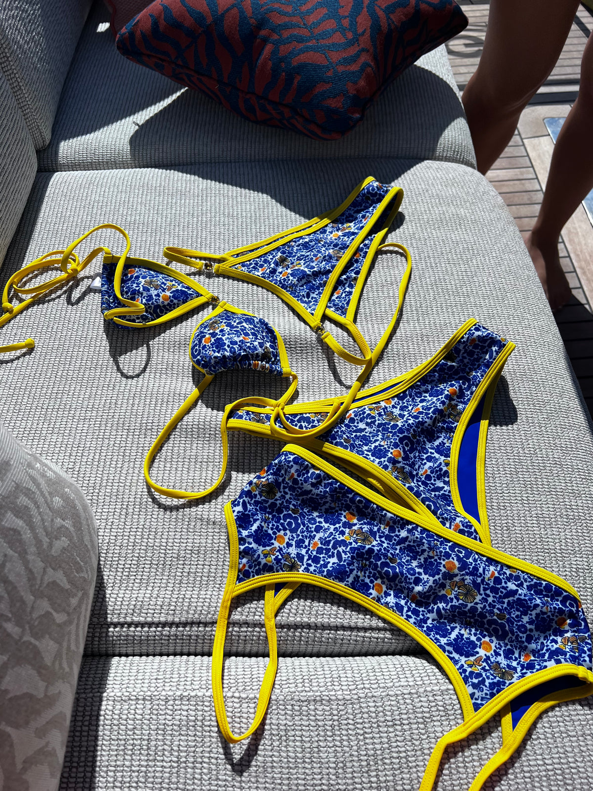 The Ophelia Bikini, a stunning statement piece that radiates vibrant energy. Featuring a classic blend of Mediterranean blue, vibrant yellow, and crisp white, this bikini is adorned with a bold floral print that evokes the beauty of Greece. The eye-catching yellow gemstone accents and matching straps add a touch of elegance. With its flattering fit and stylish design, this bikini is perfect for making a splash at the beach or pool this summer!