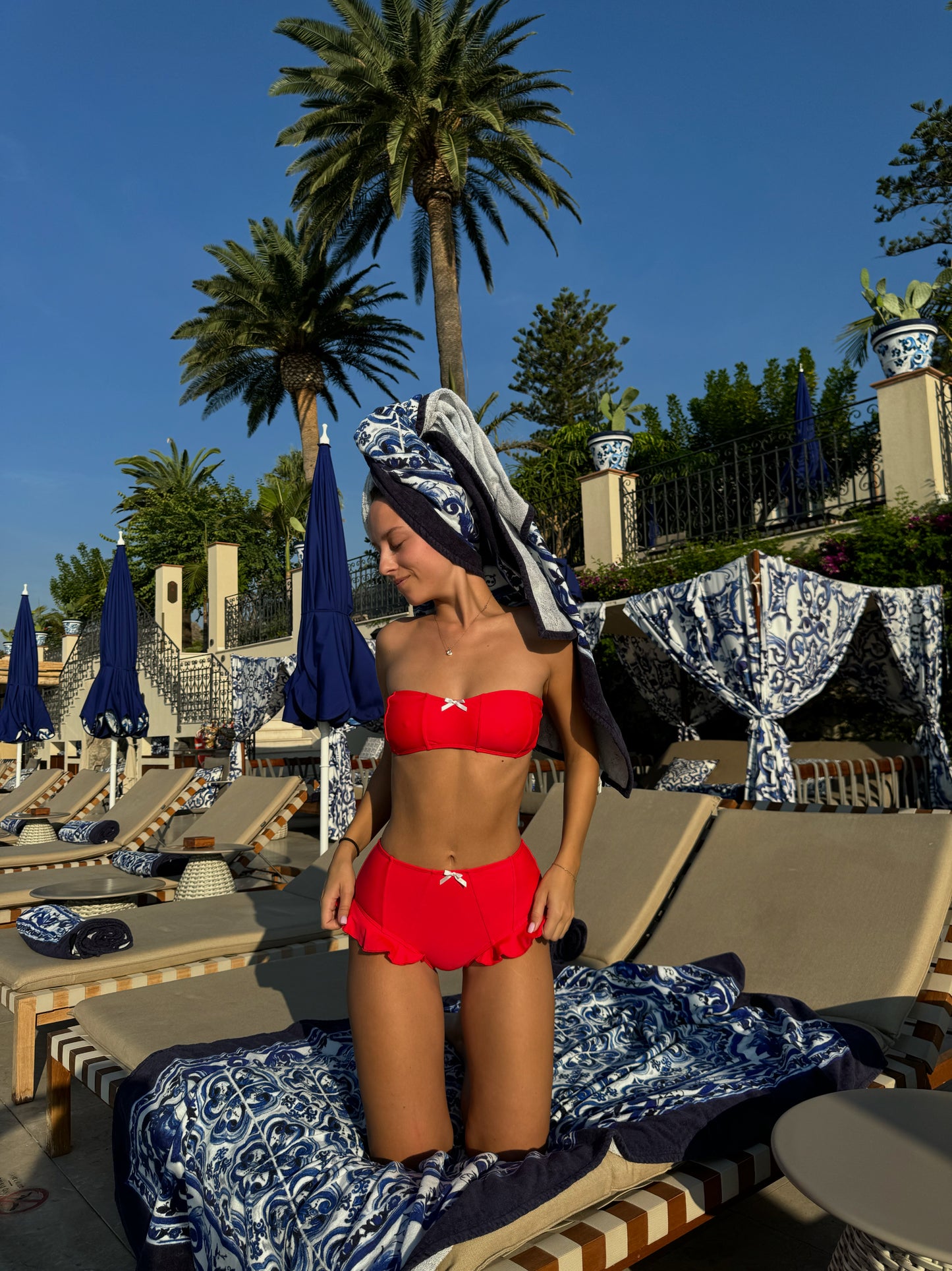 The Fitzgerald Bikini, a stunning vintage-inspired red bikini set that exudes confidence and charm. The bandeau-style top features a playful white bow detail, complemented by a tie-back design for a secure fit. The high-waisted bottoms provide ample coverage and are adorned with a delightful ruffle edge, adding a flirty touch. Perfect for sun-soaked days, this timeless bikini combines retro flair with modern comfort, making it an essential addition to your summer wardrobe!