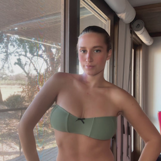 The Rosemary Bikini, a vintage-inspired swimwear piece with a modern twist. This beautiful sage green bikini features charming bow details that add a playful touch while remaining neutral and flattering. The bandeau top showcases a minimalist tie-back design for a comfortable fit, while the high-waisted bottoms feature elegant ruffle detailing, enhancing your silhouette. Versatile and stylish, the Rosemary Bikini is perfect for making a statement at the beach or pool!